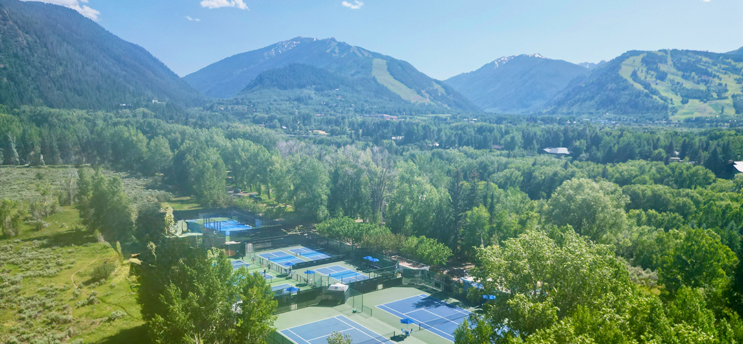 Blue tennis court with white court lines and a mountainside view