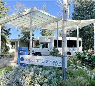 The entrance to Aspen Meadows Hotel, with a transportation shuttle parked nearby