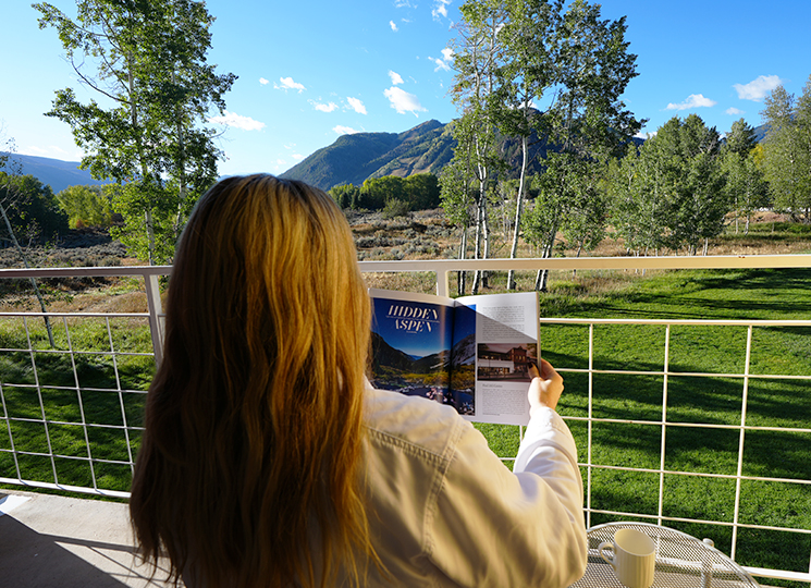 Woman reads magazine on balcony overlooking mountain vistas