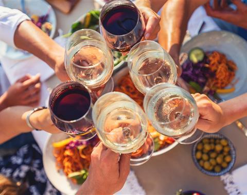 A group of wine glasses cheering above an assortment of food