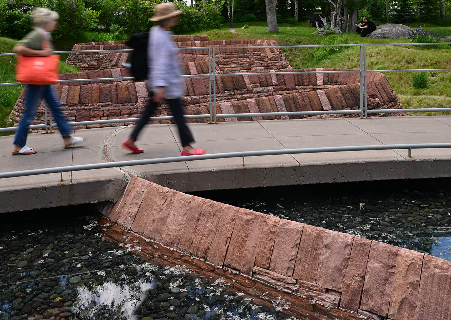 Stone river functional sculpture and people walking across bridge